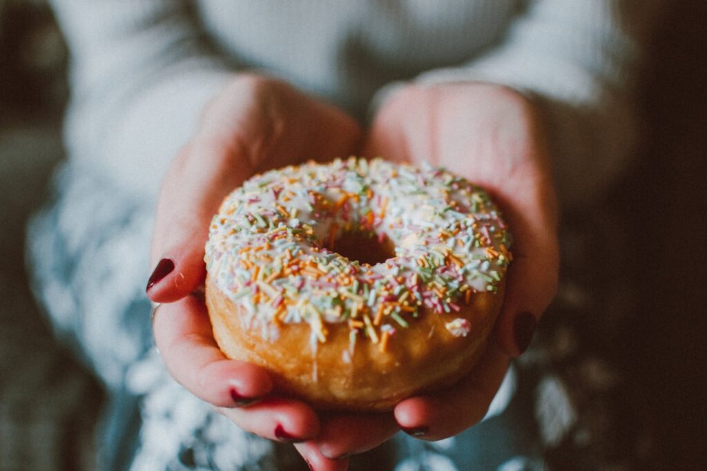 pexels-photo-1785852 Close-up photo of a donut with colorful sprinkles held in hands, ideal for food and indulgence themes.